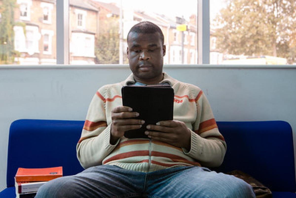 A man in a cream jumper reads from a tablet device.