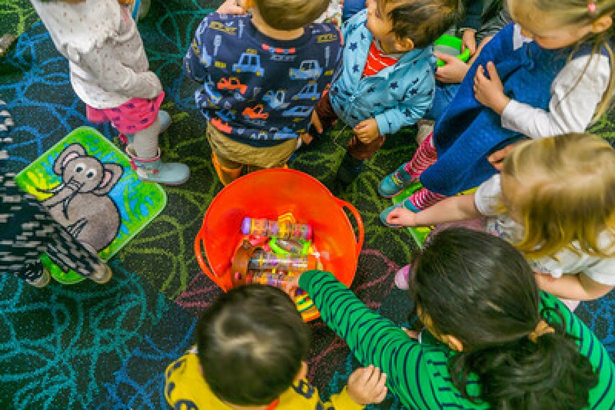 A circle of children play with toys in an orange bucket