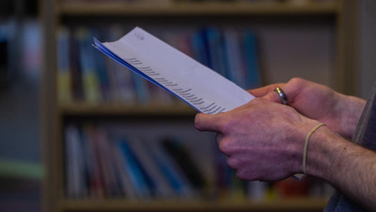 A pair of hands hold a sheet with printed writing on it