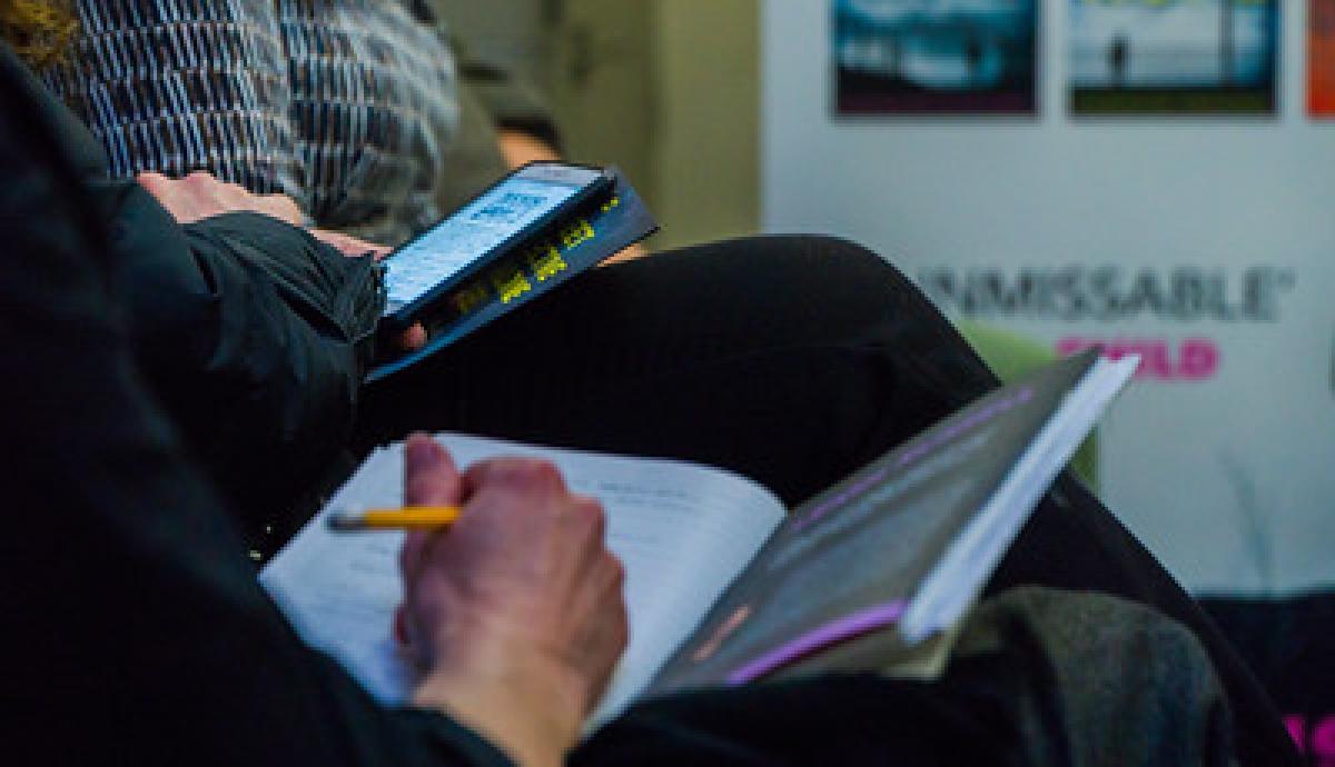 A hand holding a yellow pencil rests on an open leaflet