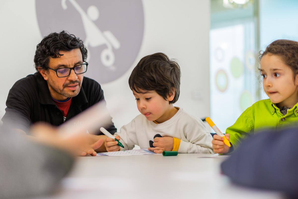 Man helping two children working at a table in a library