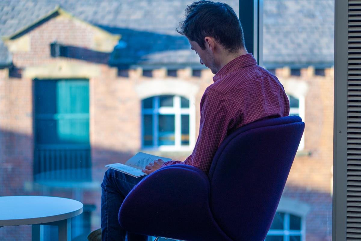 A seated man reads a book in a library