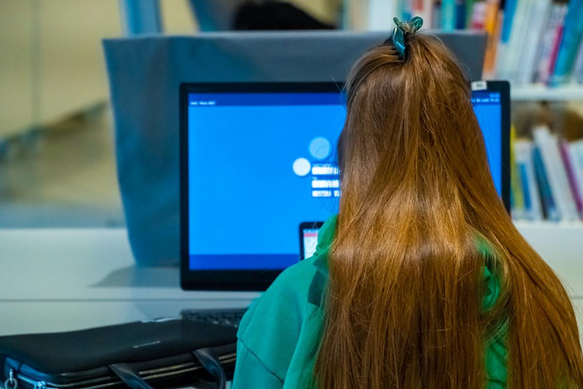 The back of a young girl&#039;s head as she works at a computer screen in a library