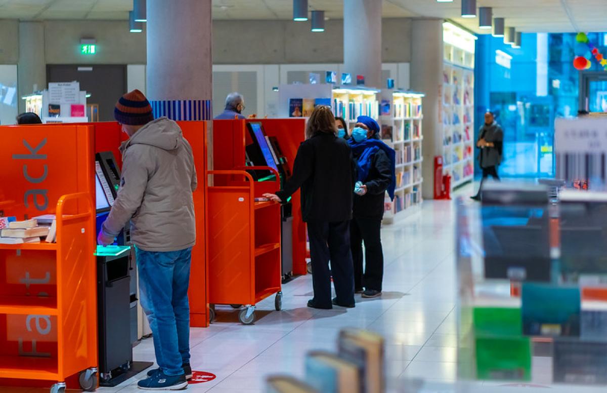 A group of people use red return shelves in a library.