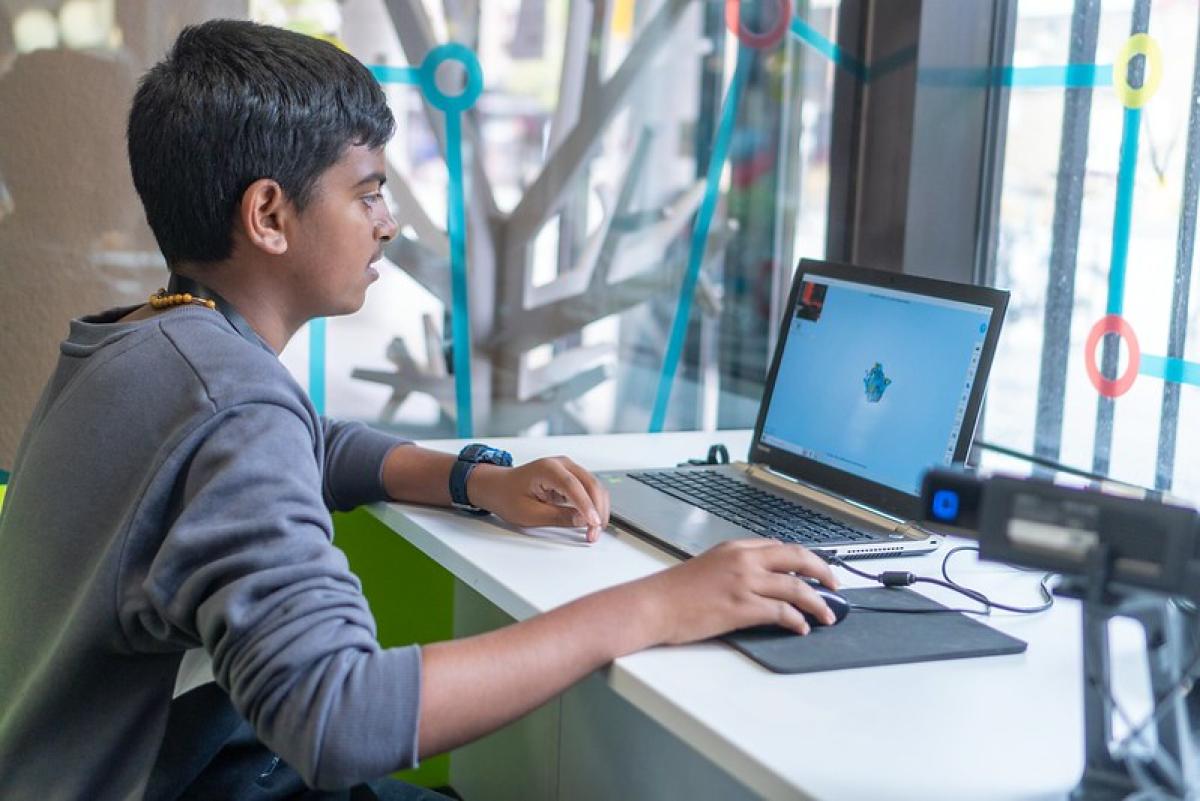 A boy sits working at a laptop in a library.