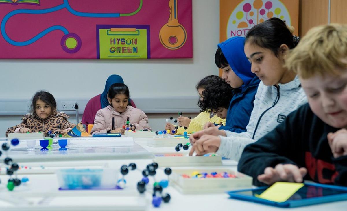 Children sit around a table in a library engaged in arts and crafts.