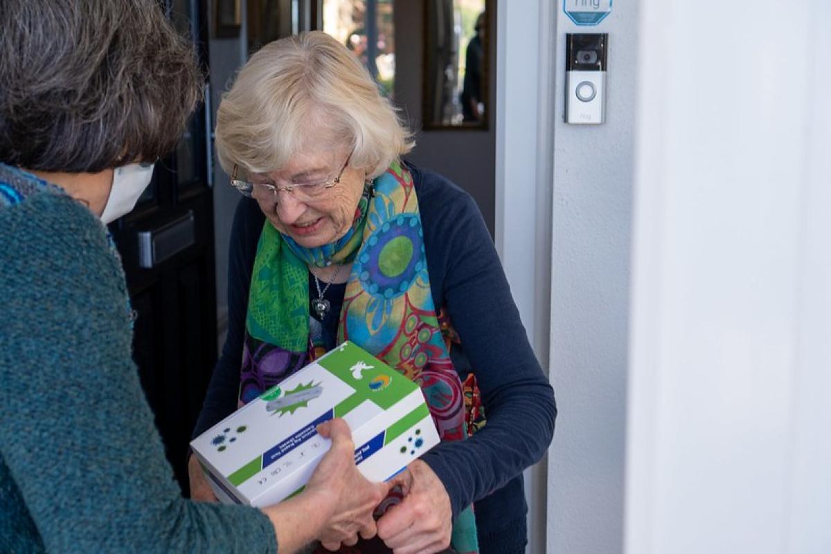 A woman hands over a box to another woman who is smiling as she receives it