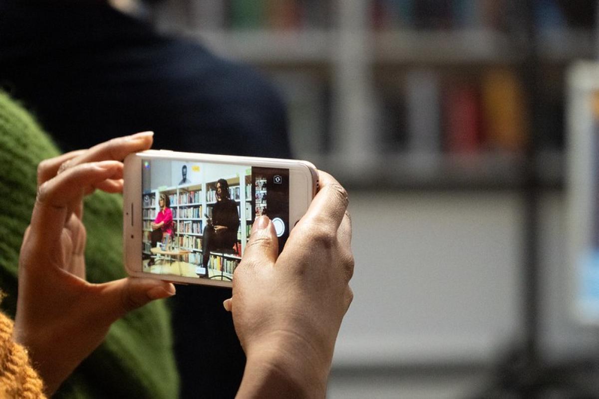 A smartphone captures an event in a library. The event is in progress and is being shown on the smartphone screen.