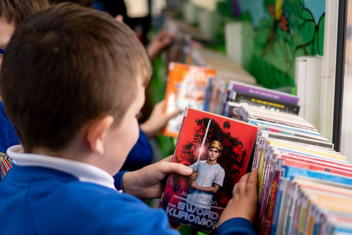 A schoolboy smiles as he looks at the cover of a book in a library.