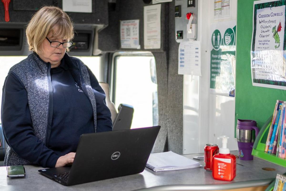 A female librarian works at a laptop whilst standing up.