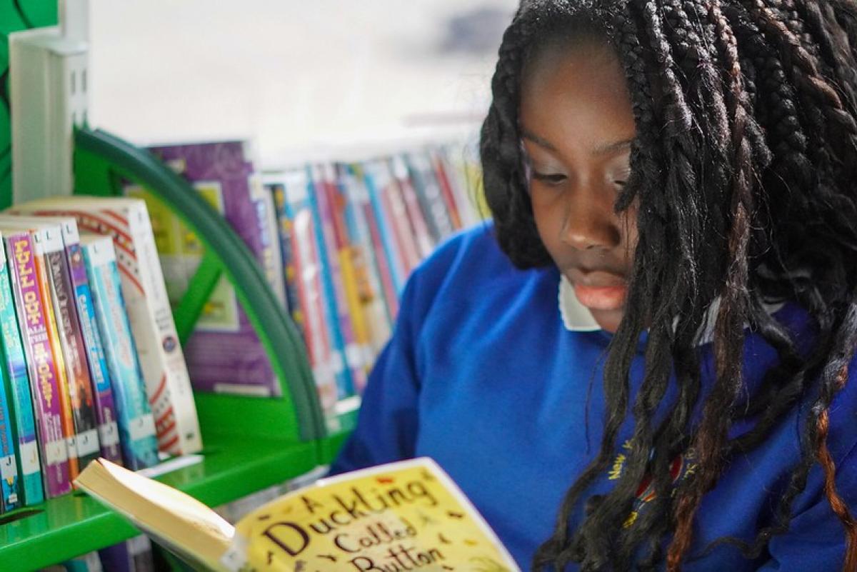 A girl dressed in a blue school sweatshirt concentrates as she reads a book