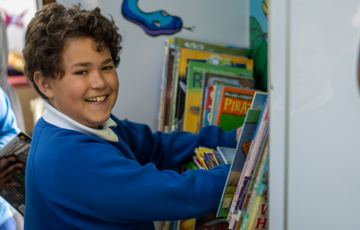 A boy smiles at the camera while browsing for books in a children&#039;s library