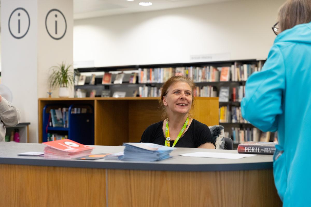 A female librarian welcomes a customer. 