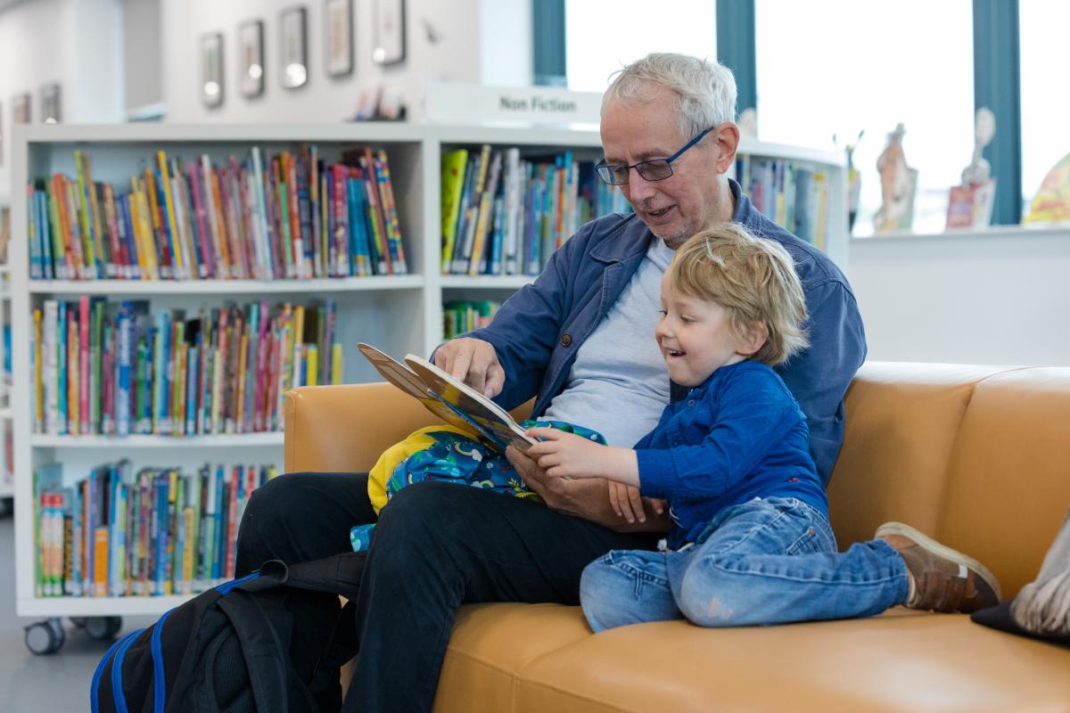 An older man reads a book to a smiling child.