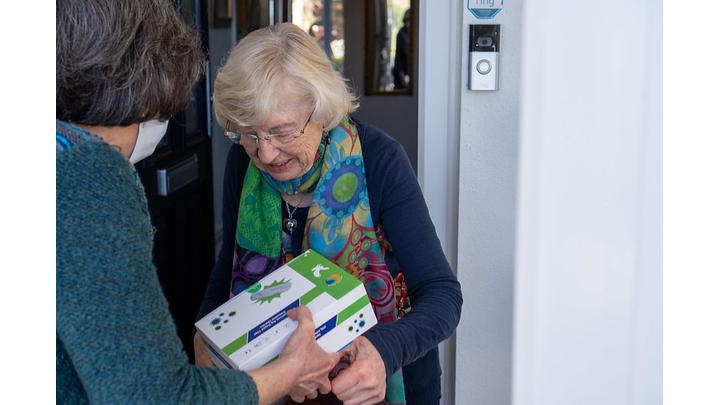 An older woman smiles as she receives a package from a librarian.