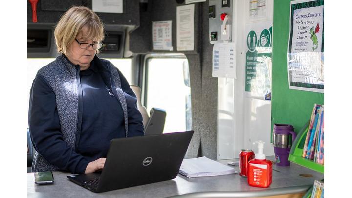 A female librarian works at a laptop whilst standing up.