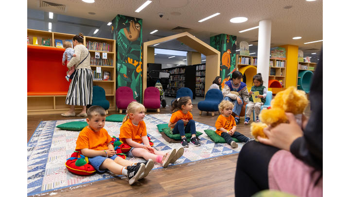 Several children dressed in orange listen to a storyteller in a library