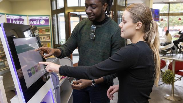 Two people interacting with a touch-screen display in a library.