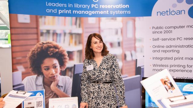Women smiling stood at a table in front of a sponsors banner