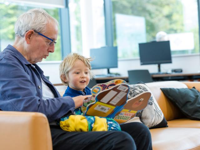 An older man reads to a young boy in a children's library.