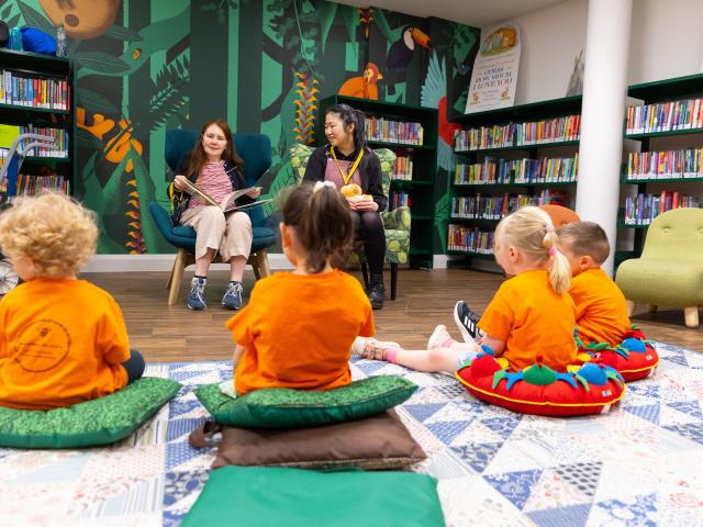 Small children listen to a woman read a story aloud in a children's library.