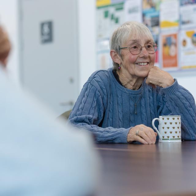 Woman smiling sitting at a table in a library with a cup of tea