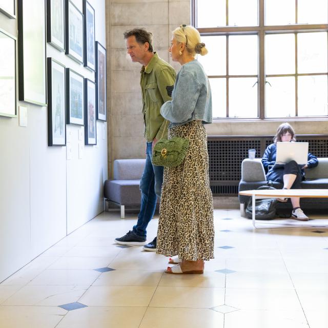 Couple looking at art prints on a wall in library foyer