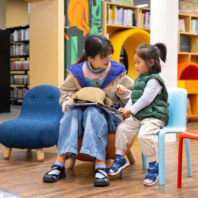 Mum and daughter sitting on chairs reading a book together in a colourful library