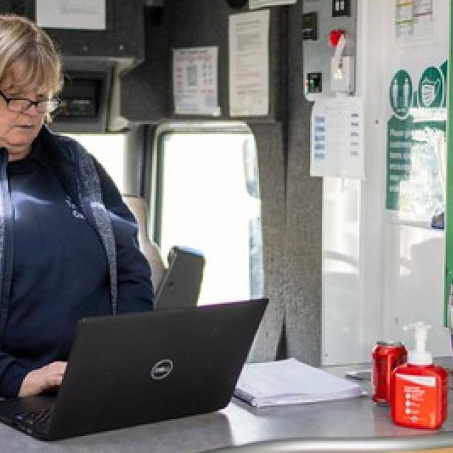 A female librarian wearing glasses studies a laptop screen.