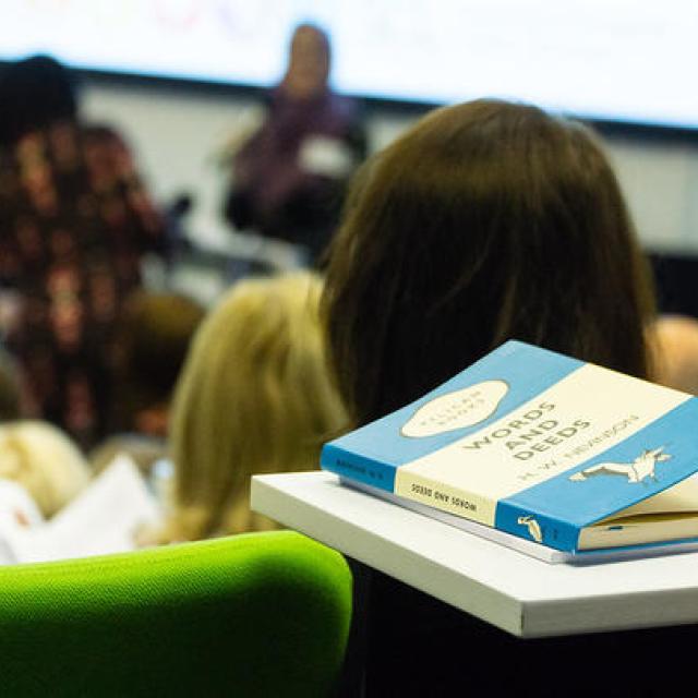 A Penguin paperback book rests on a desk inside a conference hall.