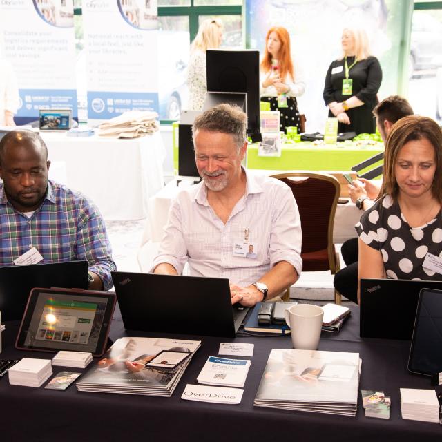 Three colleagues seated at an exhibition stall at a conference.