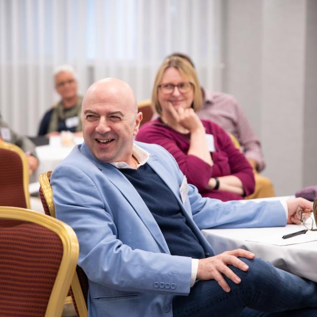 A seated man is laughing while taking part in a workshop.