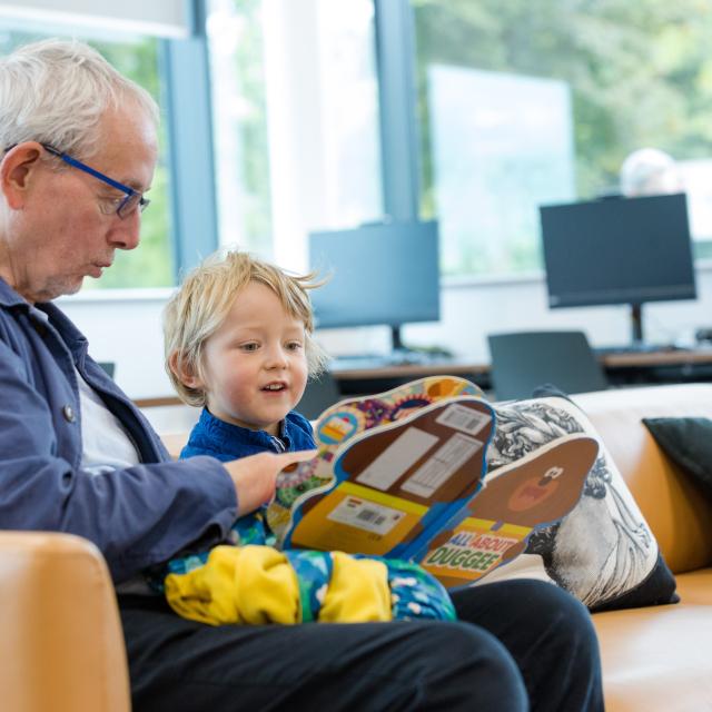 An older man reads to a young boy in a children's library.