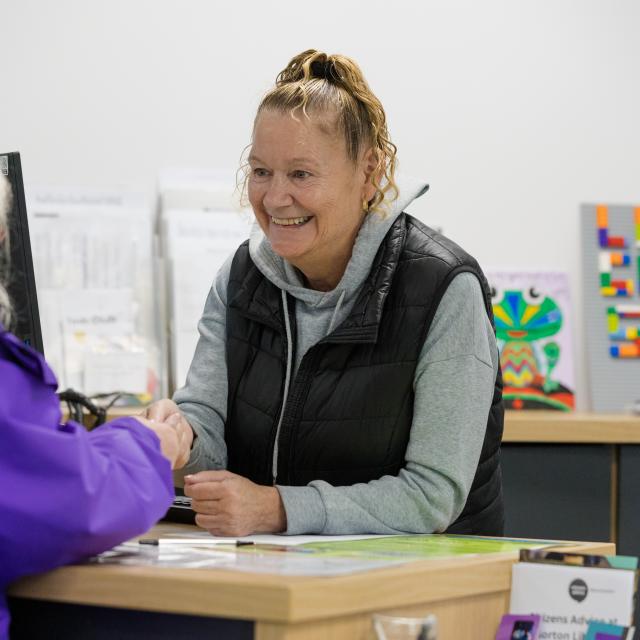 A member of library staff is serving a customer and smiling.