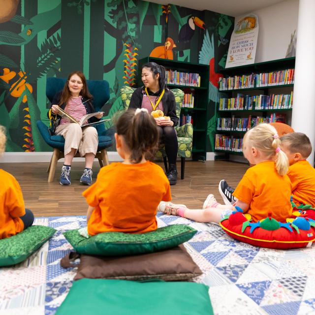 Small children listen to a woman read a story aloud in a children's library.