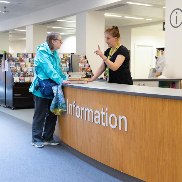 A library customer is helped by a staff member at an information desk.