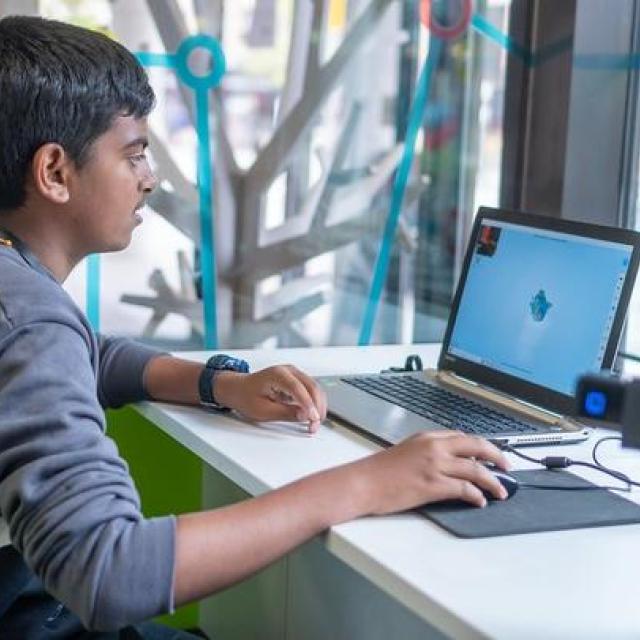 A teenage boy sits studying a laptop screen.