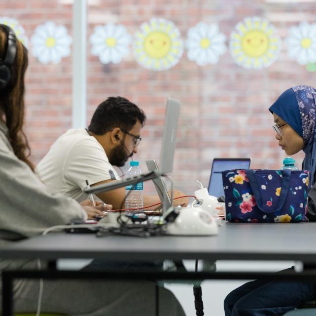 Three people sit around a table in a library working.