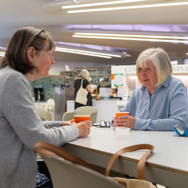 Two women discuss something at a library table.