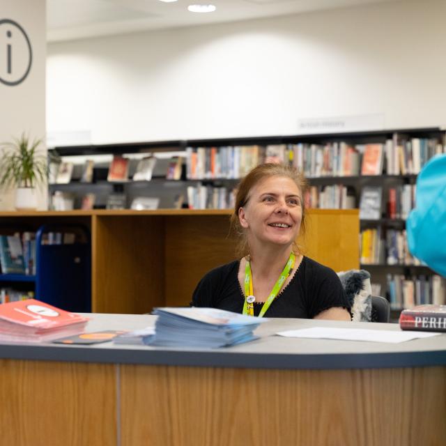 A female librarian welcomes a customer. 