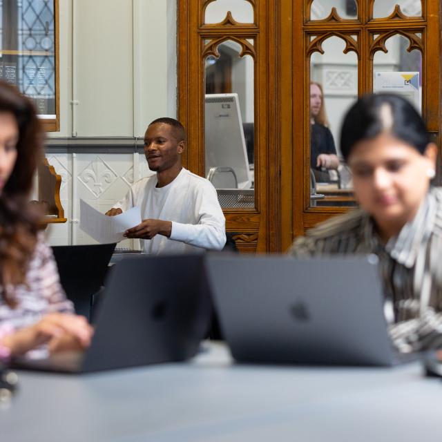 Two women work at laptops; a man is in the background.