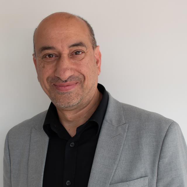 Libraries Connected Past President Ayub Khan is dressed in a black shirt and grey jacket.