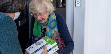 An older woman smiles as she receives a package from a librarian.