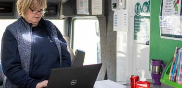 A female librarian works at a laptop whilst standing up.